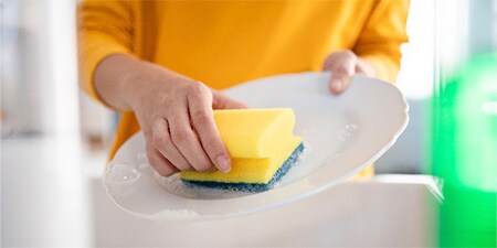 Frau spült Geschirr mit Scotch-Brite® Delicate Griffschwamm
