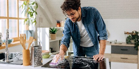 Mann reinigt die Glasherdplatte mit einem Scotch-Brite™ Glaskeramik-Reinigungsschwamm
